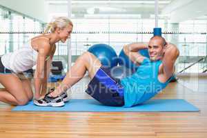 Trainer assisting young man with abdominal crunches at fitness s