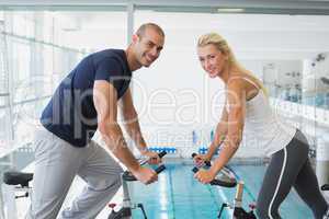 Side view of smiling couple working on exercise bikes at gym