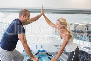 Fit couple giving high five while working on exercise bikes at g