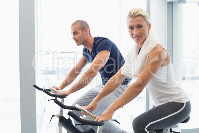 Fit couple working on exercise bikes at gym