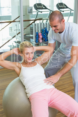 Trainer assisting woman with abdominal crunches at gym