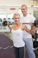 Male trainer helping woman with lifting barbell in gym