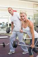Sporty young couple lifting barbells in gym