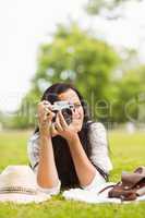 Smiling brunette lying on grass taking picture