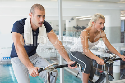 Determined couple working on exercise bikes at gym