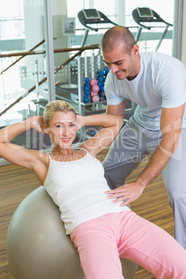 Trainer assisting woman with abdominal crunches at gym