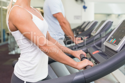 Side view mid section of couple running on treadmills at gym