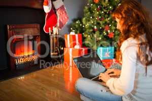 Redhead woman sitting on floor using laptop at christmas
