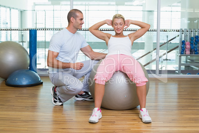 Male trainer assisting woman with abdominal crunches at gym