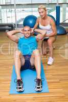 Trainer assisting man with abdominal crunches at fitness studio
