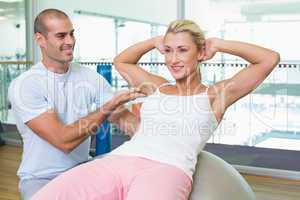 Trainer assisting woman with abdominal crunches