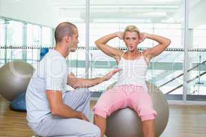 Trainer assisting woman with abdominal crunches at gym