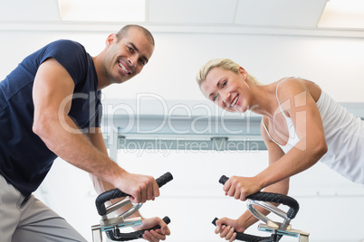 Fit couple working on exercise bikes at gym