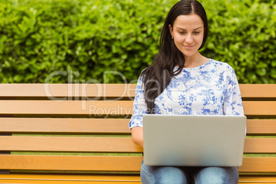 Smiling brunette using laptop on bench