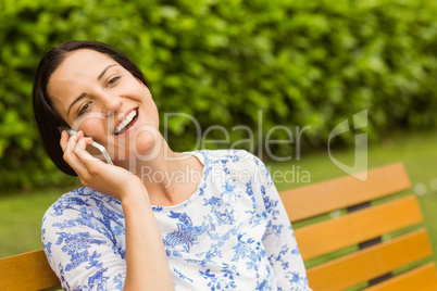 Smiling brunette sitting on bench phoning