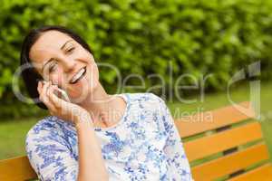 Smiling brunette sitting on bench phoning
