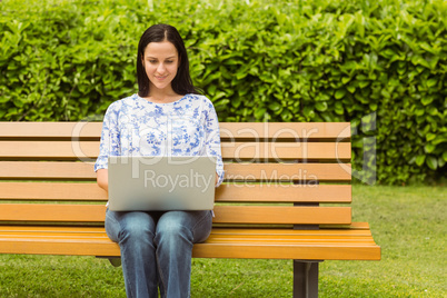 Smiling brunette sitting on bench using laptop