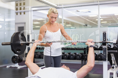 Trainer helping man with lifting barbell in gym