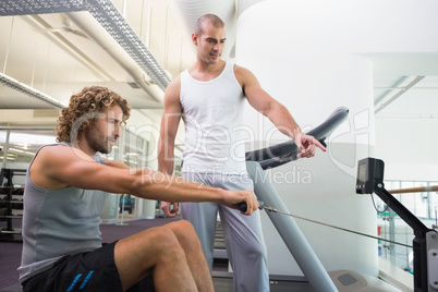 Male trainer assisting man on fitness machine at gym