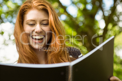 Cheerful female student reading book in park