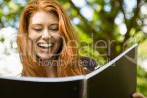 Cheerful female student reading book in park