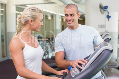 Trainer assisting woman with treadmill screen options at gym