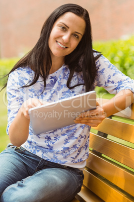 Smiling brunette sitting on bench using tablet