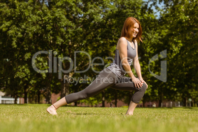 Pretty athletic redhead stretching in park