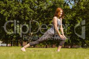 Pretty athletic redhead stretching in park