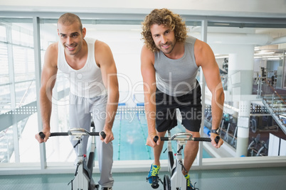 Fit men working on exercise bikes at gym