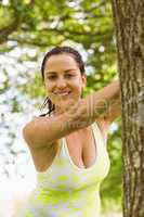 Smiling fit brunette stretching against a tree
