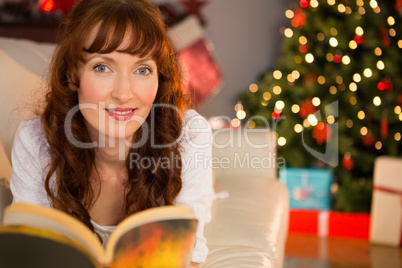 Pretty woman lying on a cosy couch reading book