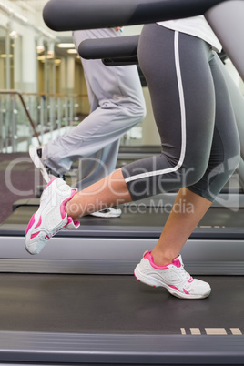 Low section of couple running on treadmills at gym