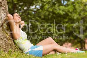 Smiling fit brunette sitting and relaxing against a tree