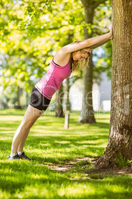 Fit blonde stretching against a tree