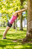 Fit blonde stretching against a tree