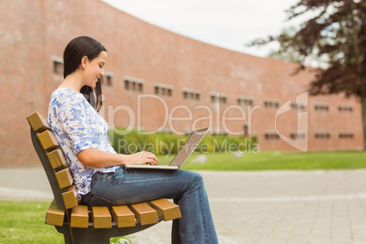 Happy brunette sitting on bench typing on laptop