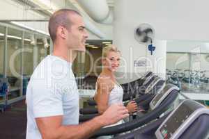 Side view of couple running on treadmills at gym