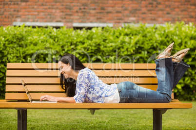 Cool brunette lying on bench using laptop