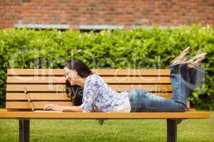 Cool brunette lying on bench using laptop