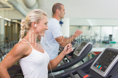 Side view of couple running on treadmills at gym