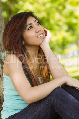 Beautiful woman sitting against tree in park