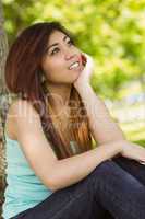 Beautiful woman sitting against tree in park