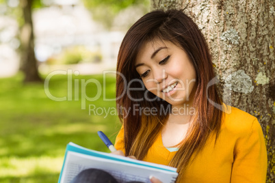 College student doing homework against tree in park
