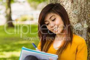 College student doing homework against tree in park