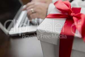 White Gift Box with Red Bow Near Man using Laptop