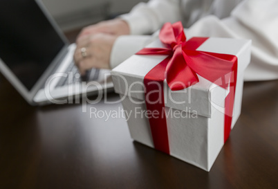 White Gift Box with Red Bow Near Man using Laptop