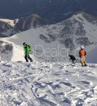Snowboarders and skier on off-piste slope in sun evening