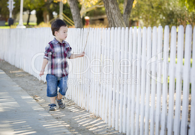 Young Mixed Race Boy Walking with Stick Along White Fence