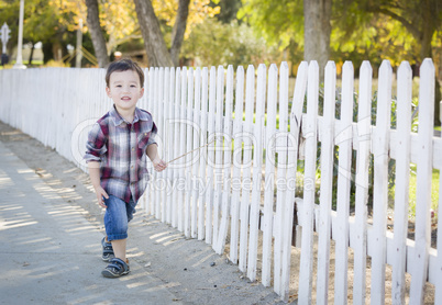 Young Mixed Race Boy Walking with Stick Along White Fence